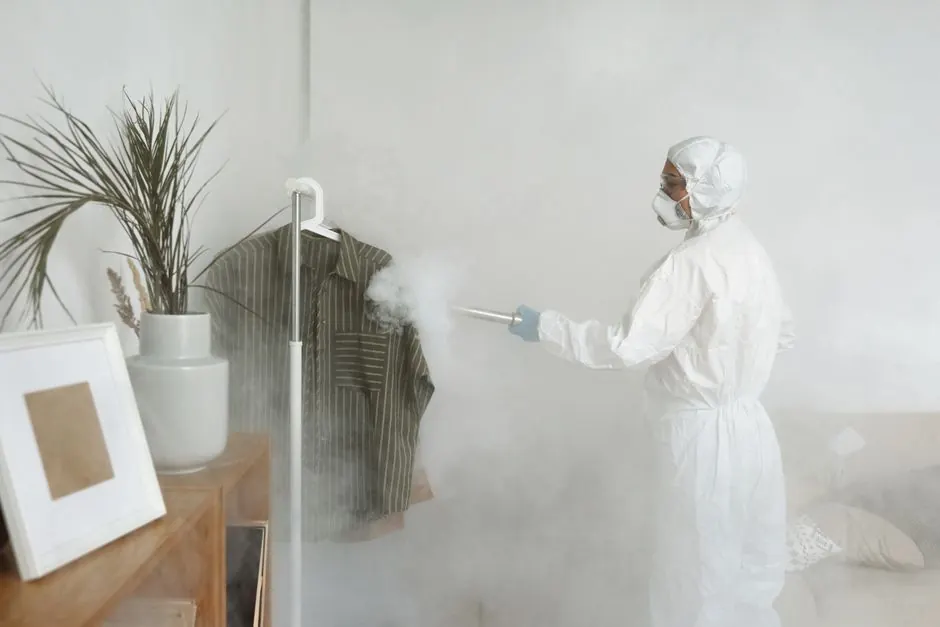 A woman in full protective gear sanitizes indoor space using a fumigation device.